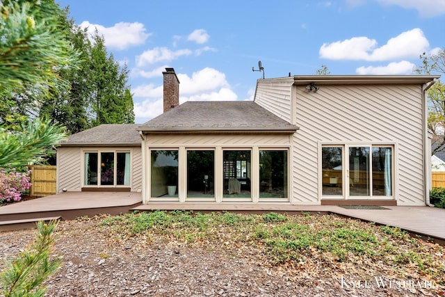 rear view of house featuring a wooden deck, a chimney, and fence