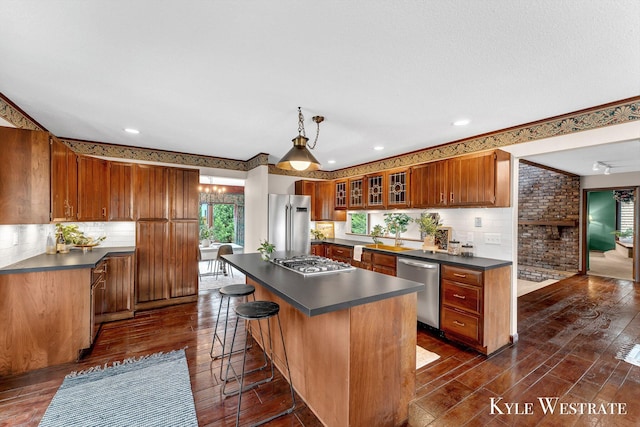 kitchen with decorative backsplash, brown cabinets, dark countertops, appliances with stainless steel finishes, and a kitchen island
