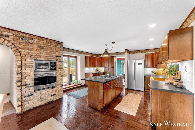 kitchen with dark countertops, appliances with stainless steel finishes, a center island, and dark wood-type flooring