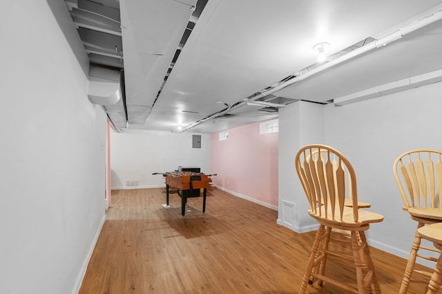 recreation room featuring wood finished floors, baseboards, and electric panel