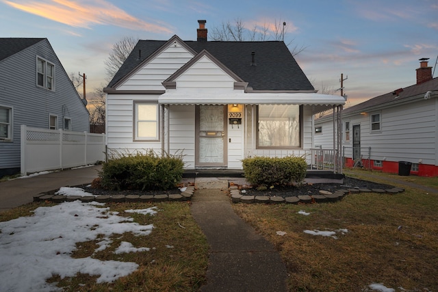 bungalow-style home with a porch, fence, roof with shingles, and a chimney