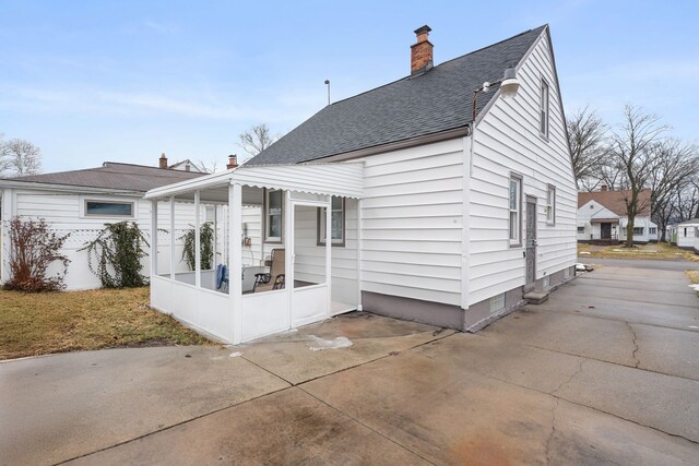rear view of house featuring roof with shingles, a chimney, and a patio