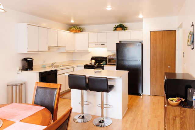 kitchen featuring a sink, light wood-type flooring, black appliances, under cabinet range hood, and light countertops