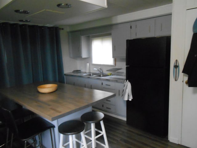 kitchen featuring a breakfast bar, freestanding refrigerator, a sink, dark wood-type flooring, and butcher block counters