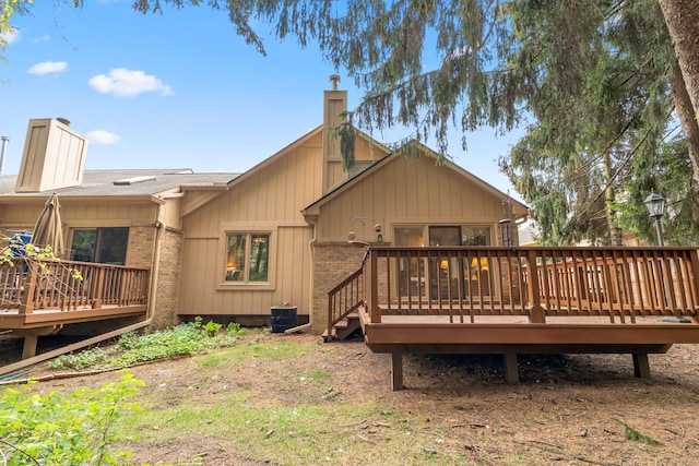 rear view of house with central air condition unit, brick siding, a chimney, and a deck