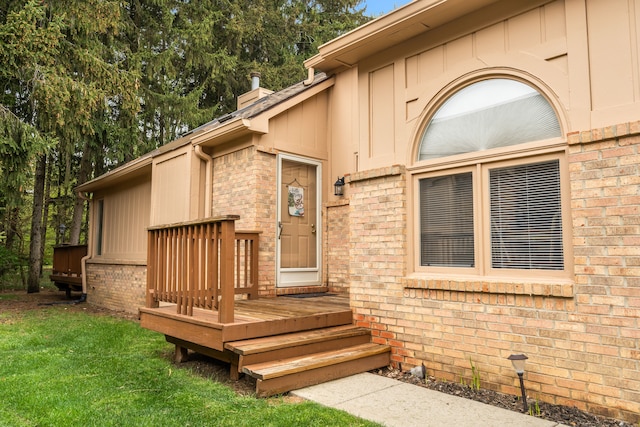 property entrance with a wooden deck, a chimney, brick siding, and a lawn