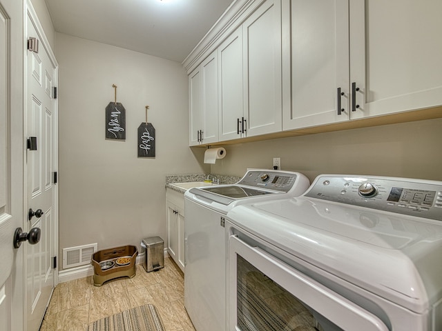 washroom with baseboards, visible vents, a sink, washing machine and clothes dryer, and cabinet space
