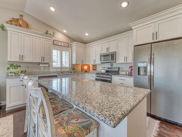 kitchen featuring a breakfast bar, a sink, white cabinetry, appliances with stainless steel finishes, and lofted ceiling
