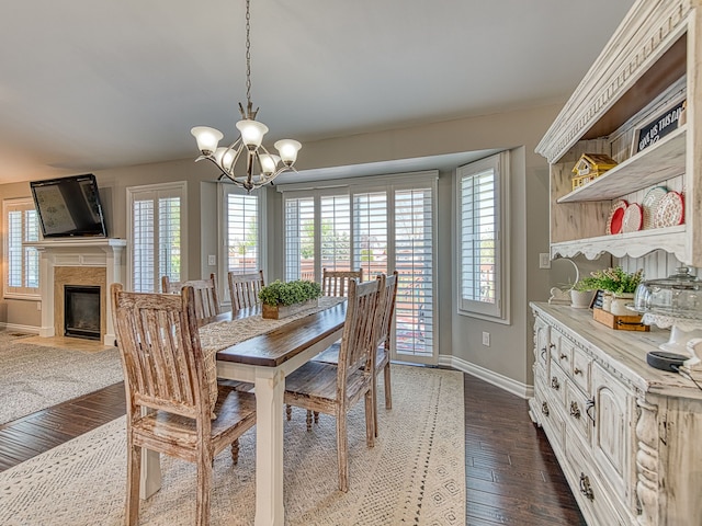 dining space with baseboards, dark wood-style flooring, an inviting chandelier, and a high end fireplace