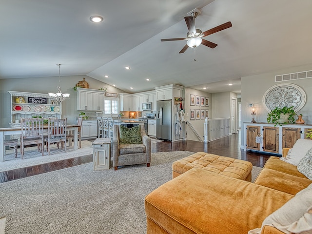 living area with vaulted ceiling, dark wood-style flooring, ceiling fan with notable chandelier, and visible vents