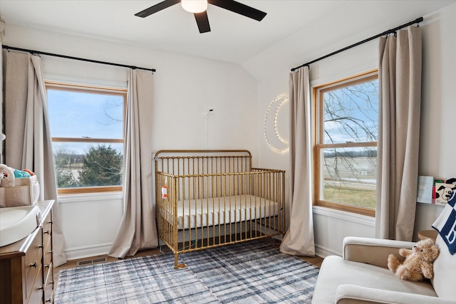 bedroom with wood finished floors, a crib, visible vents, baseboards, and lofted ceiling