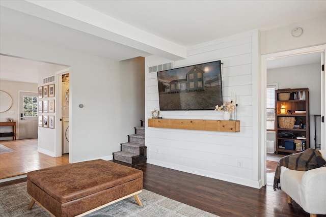 living area featuring stacked washer and clothes dryer, baseboards, visible vents, and wood finished floors
