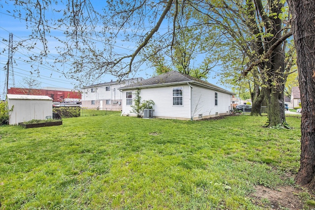 rear view of house featuring fence, an outdoor structure, central AC, and a lawn