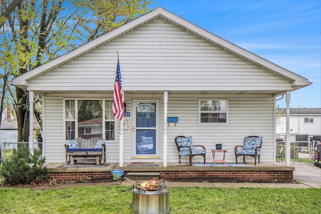 bungalow featuring covered porch, an outdoor fire pit, fence, and a front yard