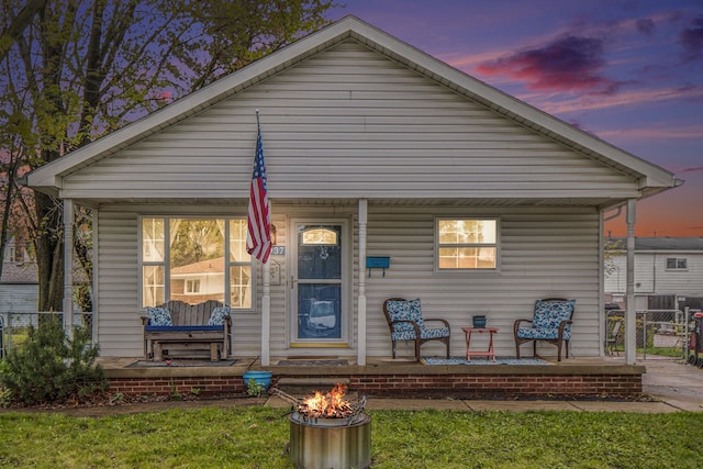 bungalow-style home featuring an outdoor fire pit, a porch, fence, and a front yard
