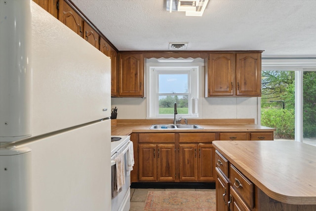 kitchen with a sink, white appliances, brown cabinets, a textured ceiling, and visible vents