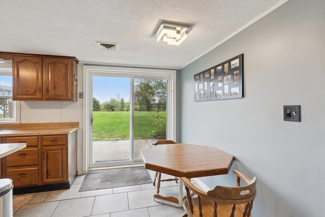 dining room with ornamental molding, a textured ceiling, light tile patterned flooring, and visible vents