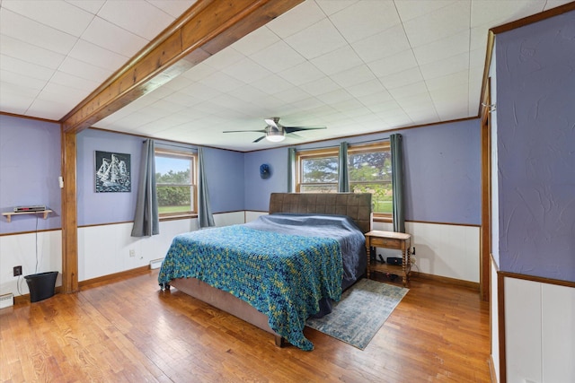 bedroom featuring multiple windows, a ceiling fan, wood finished floors, and wainscoting