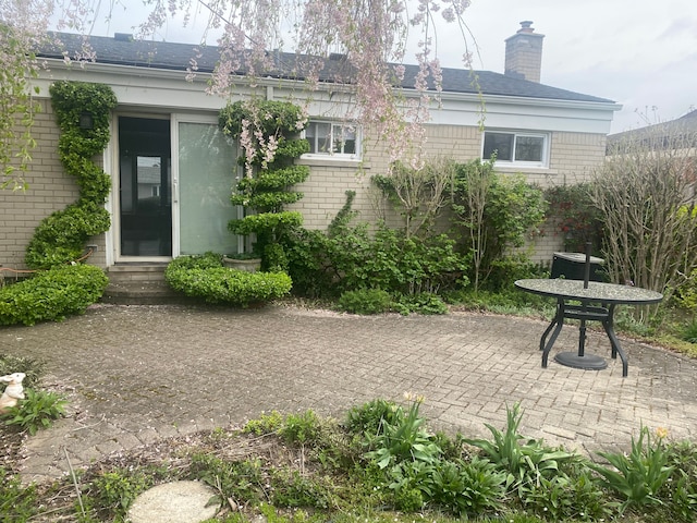 back of house featuring a patio area, a chimney, brick siding, and entry steps
