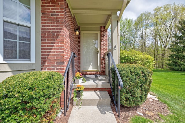 doorway to property featuring a lawn and brick siding