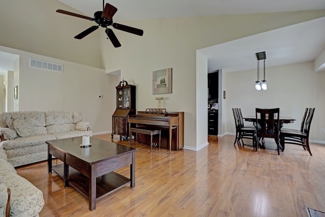 living room with light wood-type flooring, visible vents, baseboards, ceiling fan, and lofted ceiling