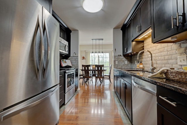 kitchen featuring a sink, dark stone counters, pendant lighting, backsplash, and appliances with stainless steel finishes
