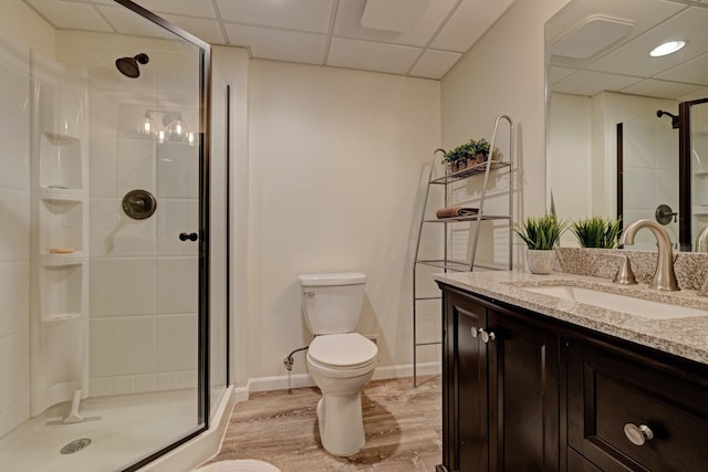 bathroom featuring toilet, wood finished floors, vanity, a shower stall, and a paneled ceiling