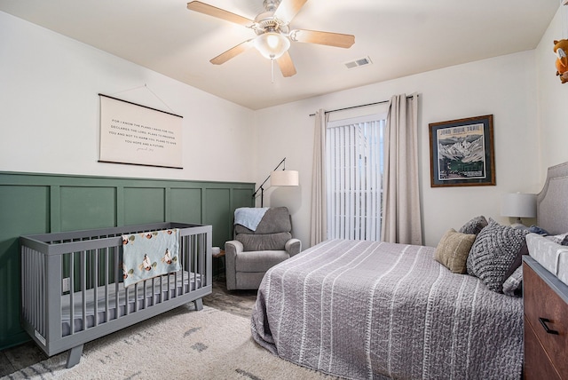 bedroom with a wainscoted wall, visible vents, a decorative wall, and ceiling fan