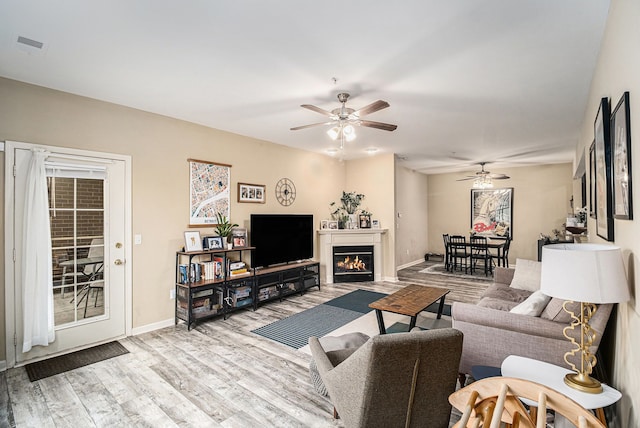 living room featuring a ceiling fan, baseboards, visible vents, a lit fireplace, and wood finished floors