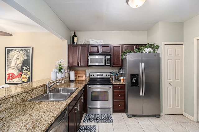 kitchen with a peninsula, light tile patterned floors, a sink, stainless steel appliances, and light stone countertops