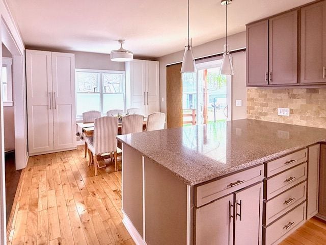 kitchen with a peninsula, light wood-type flooring, tasteful backsplash, decorative light fixtures, and light stone counters