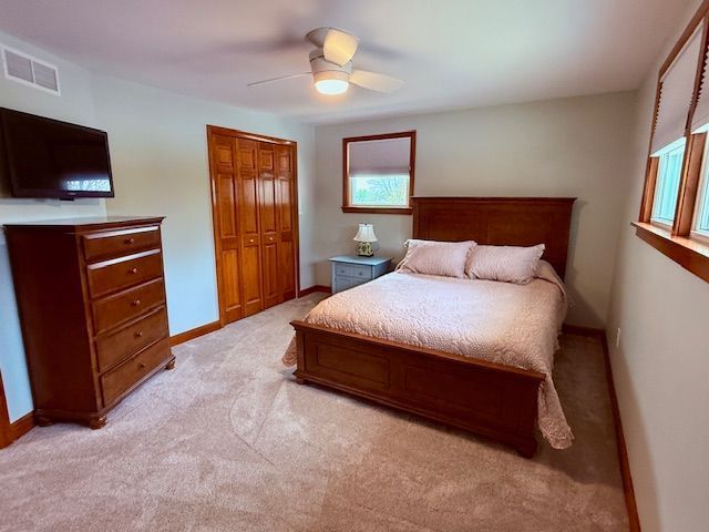 bedroom featuring a closet, visible vents, baseboards, ceiling fan, and light carpet