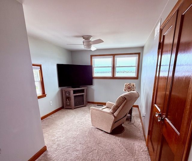 living area with light colored carpet, baseboards, and ceiling fan