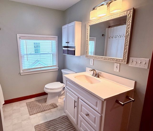 full bath featuring toilet, curtained shower, baseboards, and vanity