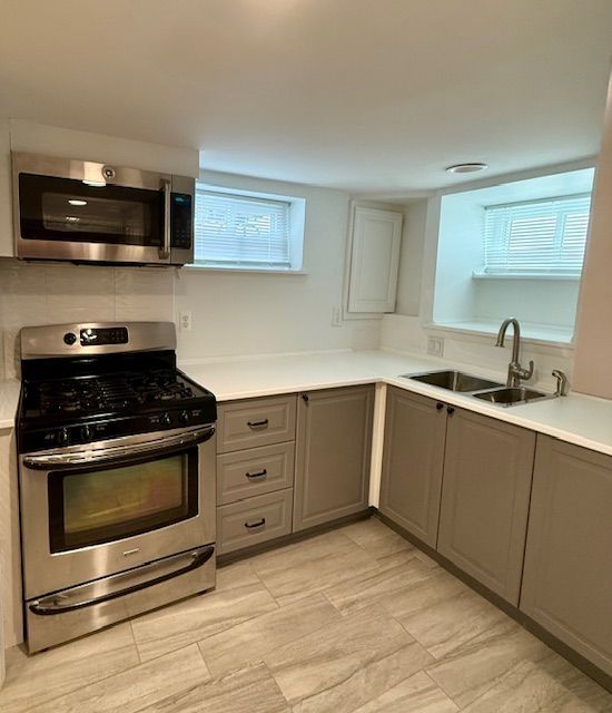 kitchen featuring light countertops, gray cabinets, stainless steel appliances, and a sink