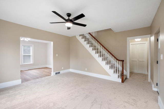 unfurnished living room featuring carpet, a ceiling fan, visible vents, baseboards, and stairway