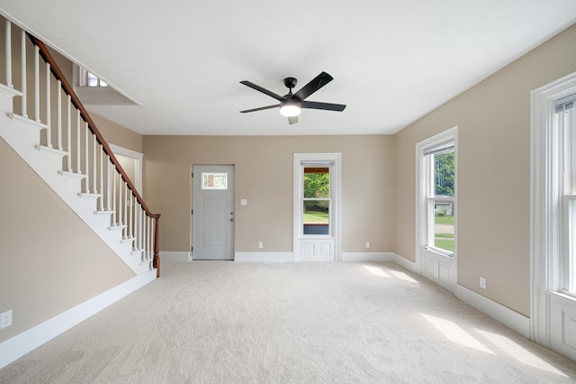 unfurnished living room with light carpet, stairs, baseboards, and a ceiling fan