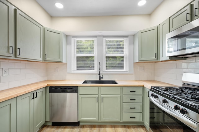 kitchen with green cabinets, wooden counters, a sink, backsplash, and stainless steel appliances