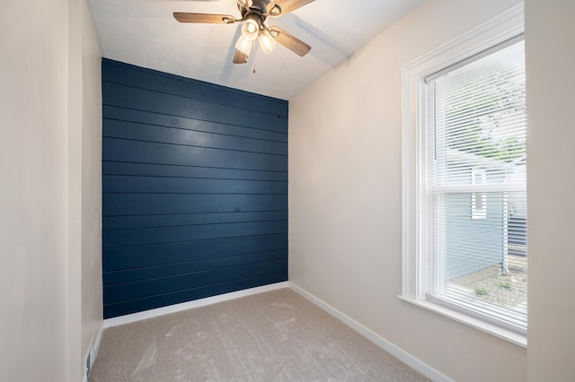 carpeted empty room with baseboards, wood walls, and ceiling fan