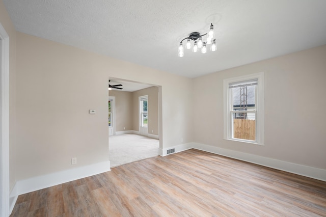 empty room with a textured ceiling, baseboards, visible vents, and light wood-style floors