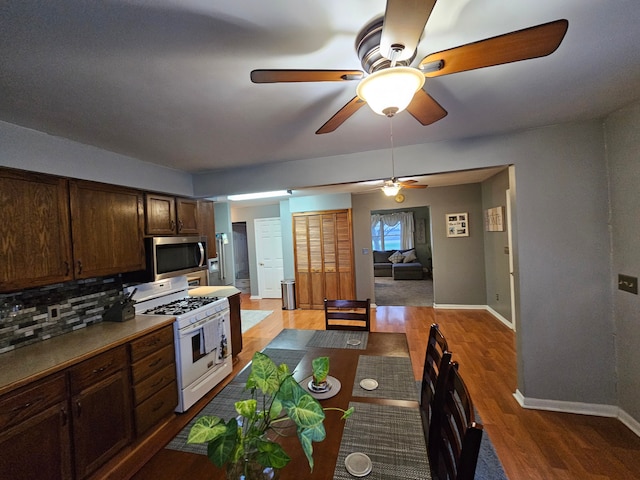 3544 Burnsline Rd, Brown City, MI 48416 - kitchen with dark brown cabinets, ceiling fan, stainless steel microwave, decorative backsplash, and white range with gas cooktop