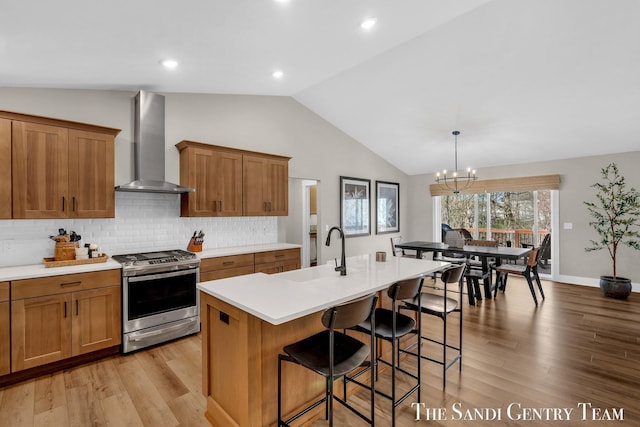 kitchen with brown cabinets, a sink, wall chimney exhaust hood, stainless steel range with gas cooktop, and vaulted ceiling
