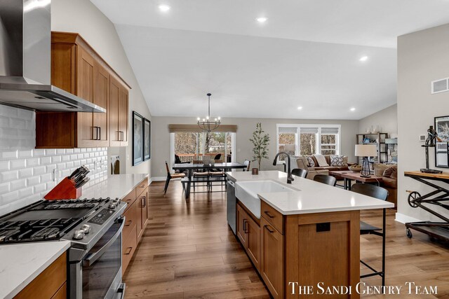 kitchen featuring a breakfast bar area, wood finished floors, a sink, stainless steel appliances, and wall chimney range hood
