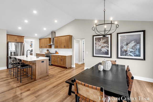 kitchen featuring light countertops, a breakfast bar, a notable chandelier, wall chimney range hood, and appliances with stainless steel finishes