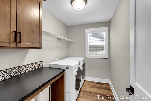 clothes washing area with baseboards, washer and dryer, visible vents, wood finished floors, and cabinet space