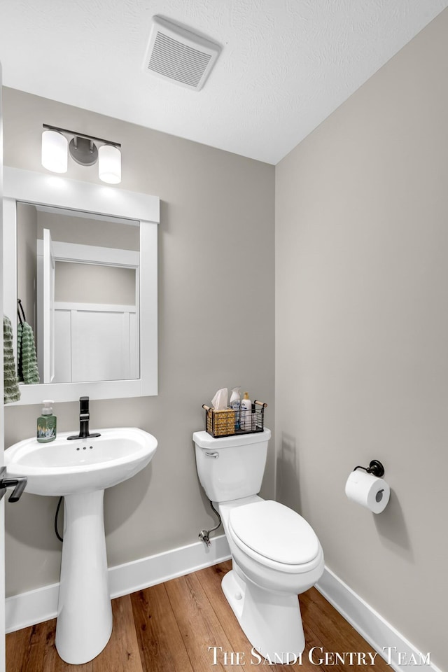 half bathroom featuring baseboards, toilet, visible vents, and wood finished floors