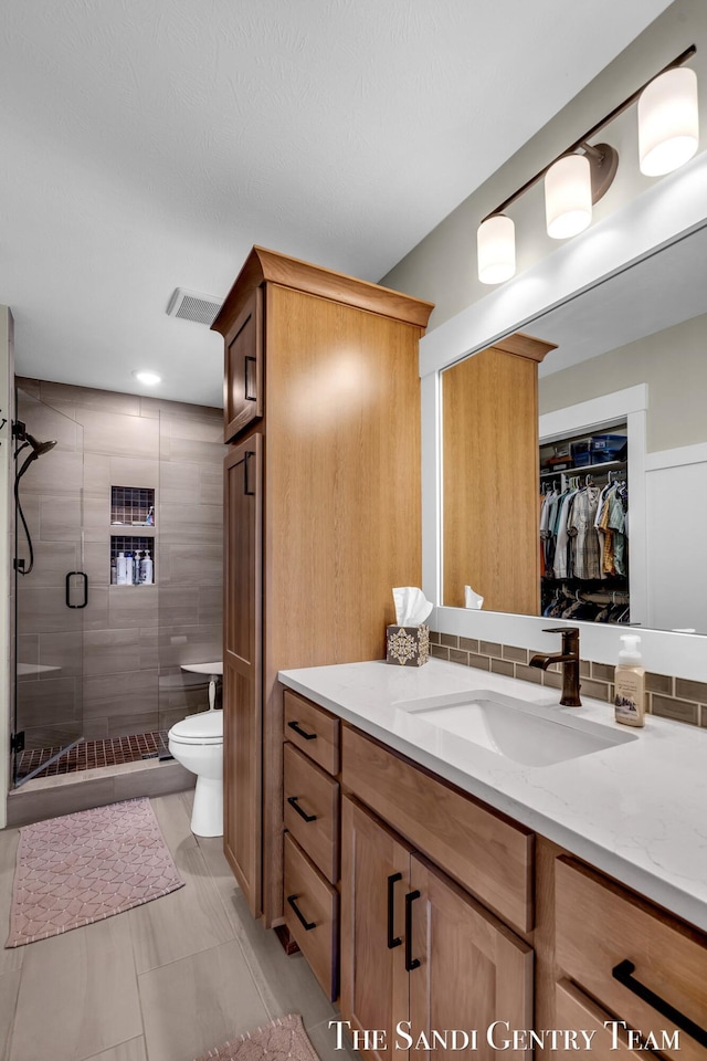 bathroom with toilet, vanity, a stall shower, a spacious closet, and decorative backsplash