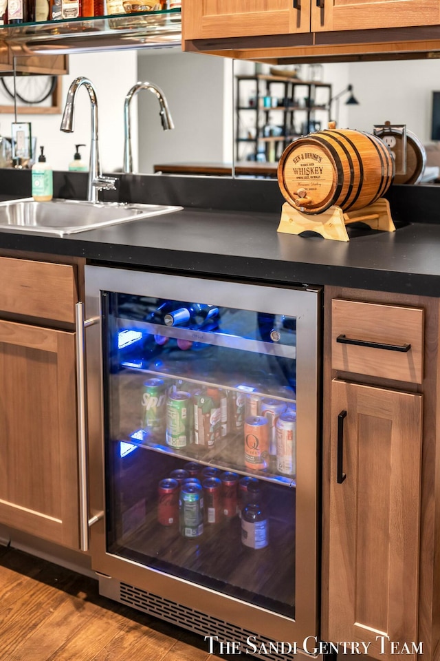bar with bar, beverage cooler, wood finished floors, and a sink