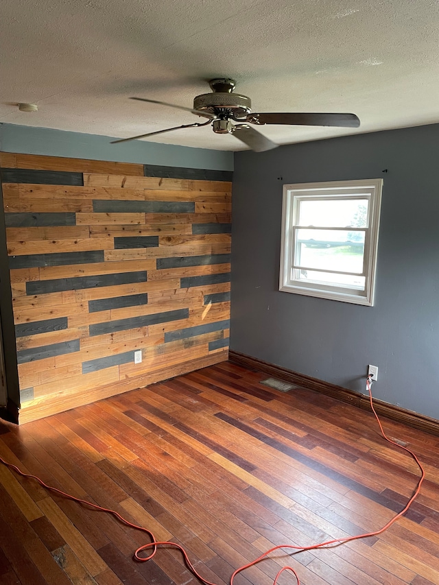 spare room featuring a textured ceiling, wooden walls, ceiling fan, and hardwood / wood-style flooring