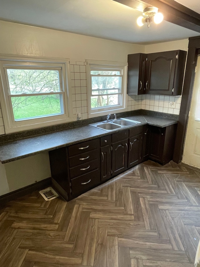 kitchen with a sink, dark brown cabinets, dark countertops, and visible vents